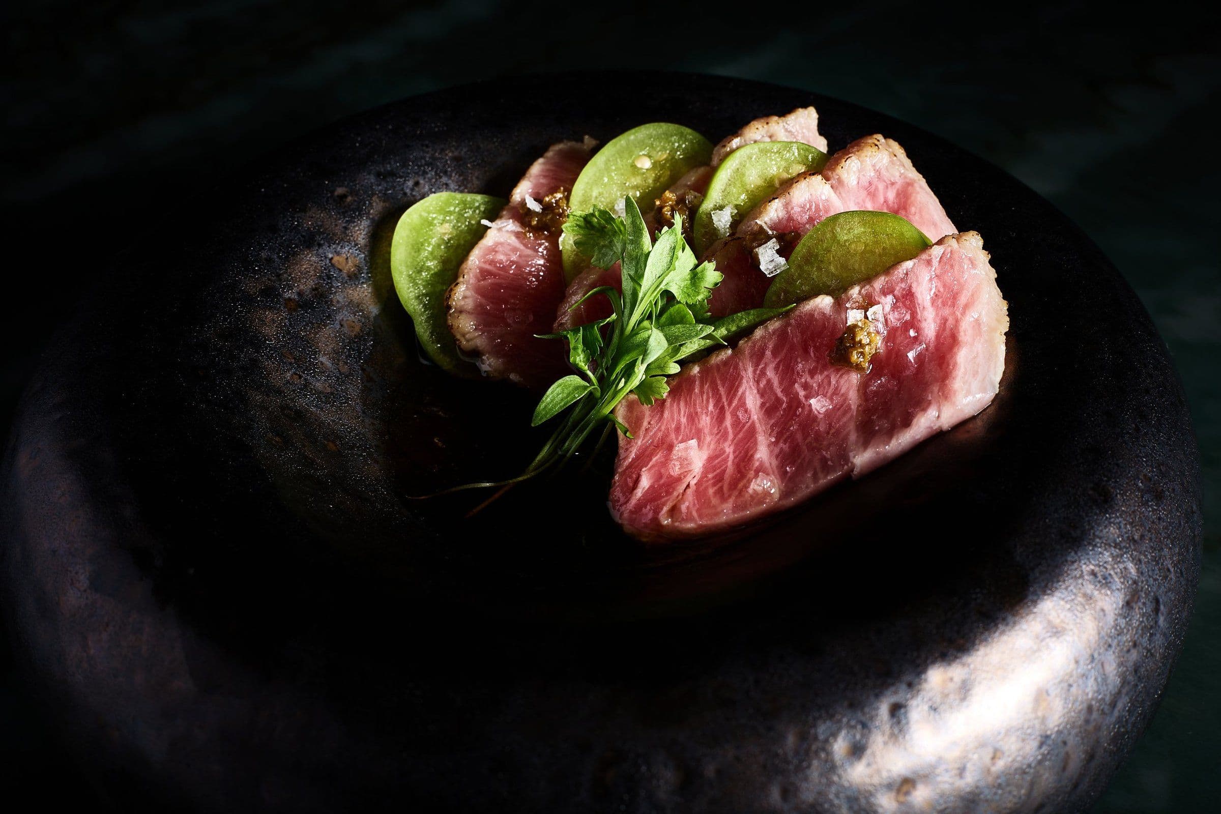 Seared wagyu with cucumber on a black plate