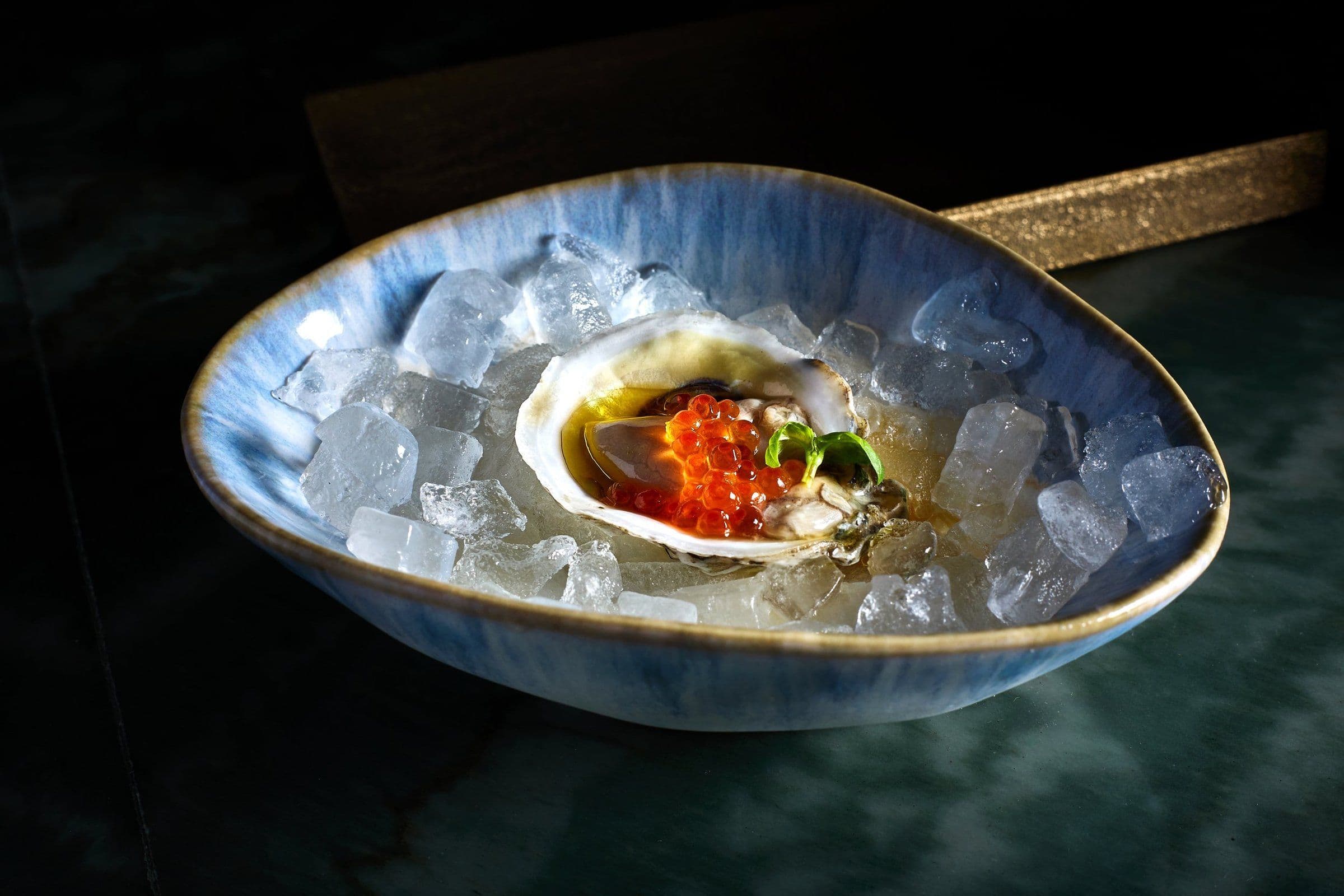 Oyster with ikura on ice in a blue ceramic dish